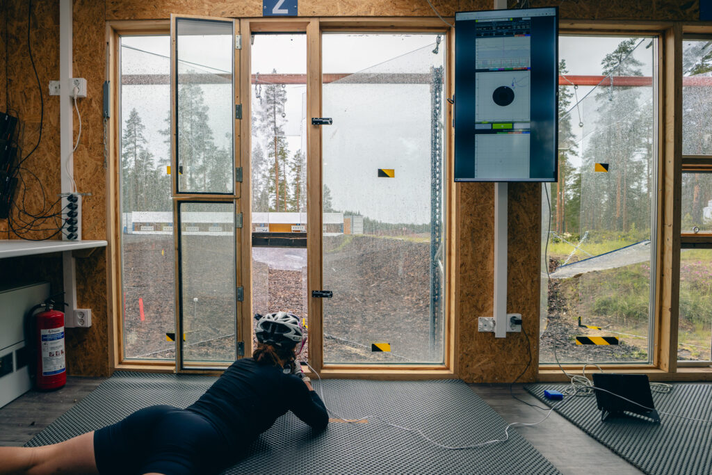 Kuvassa ampumahiihtäjä ampuu konttilabralla Vuokatissa makuuammunnassa kesäisissä maisemissa.