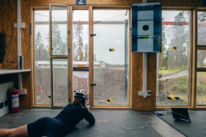 Kuvassa ampumahiihtäjä ampuu konttilabralla Vuokatissa makuuammunnassa kesäisissä maisemissa.